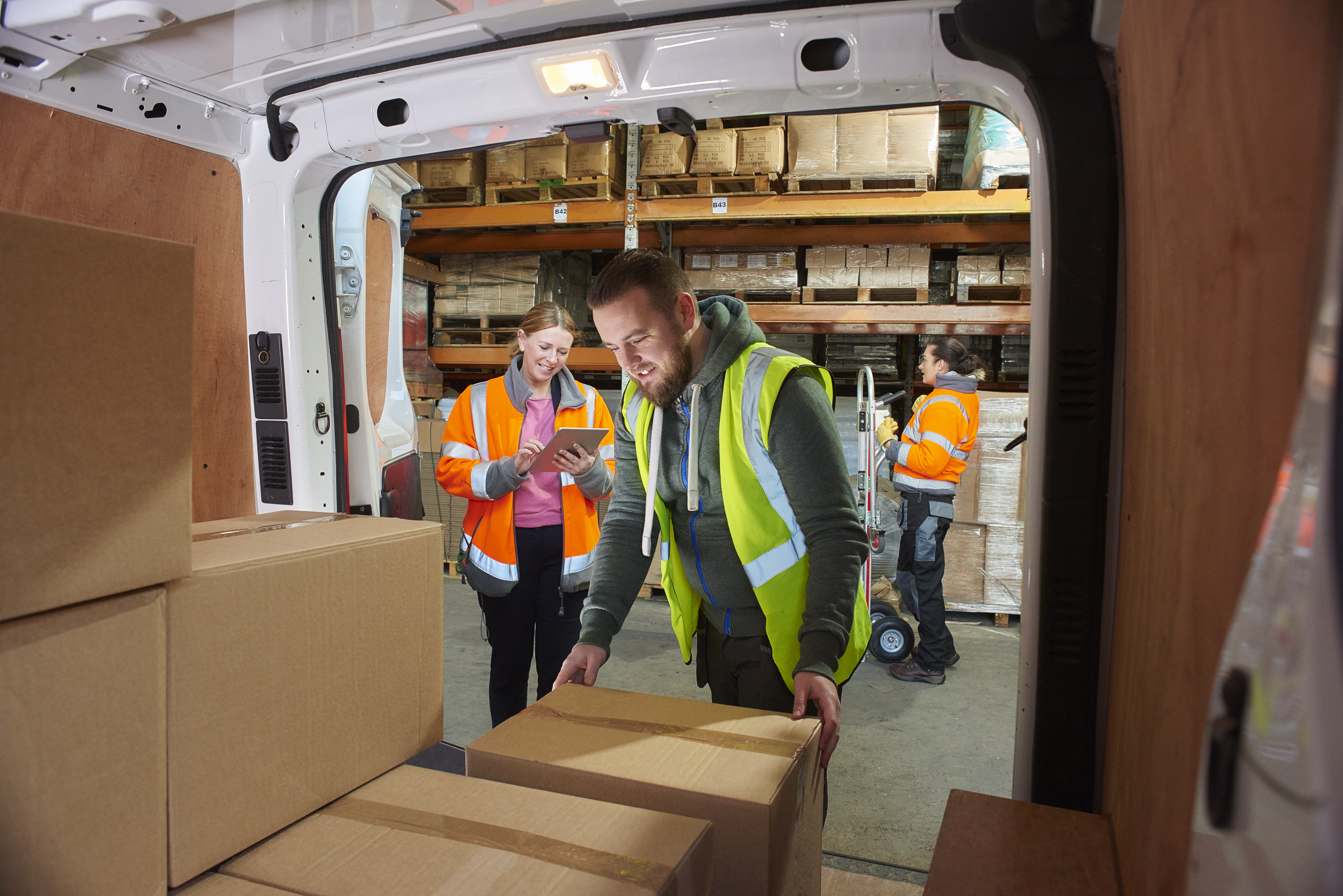 man loading parcel boxes into delivery truck with workers behind him